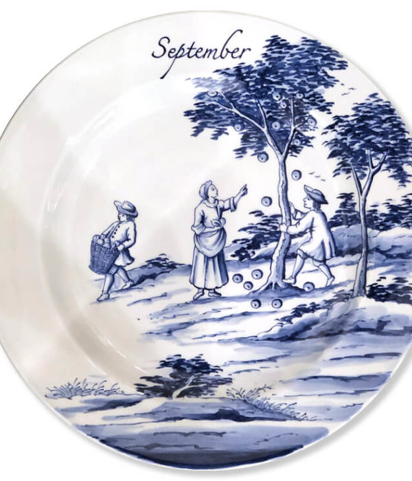 Blue and white modern Delftware plate with a woman pointing at the apples falling from a tree being shaken by a man while another man carries away a basket full of the fruit